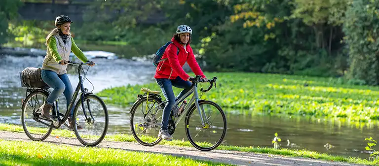 nrwt-motiv-2024-web-mobile Zwei Frauen fahren auf Fahrrädern durch die grüne Natur.
